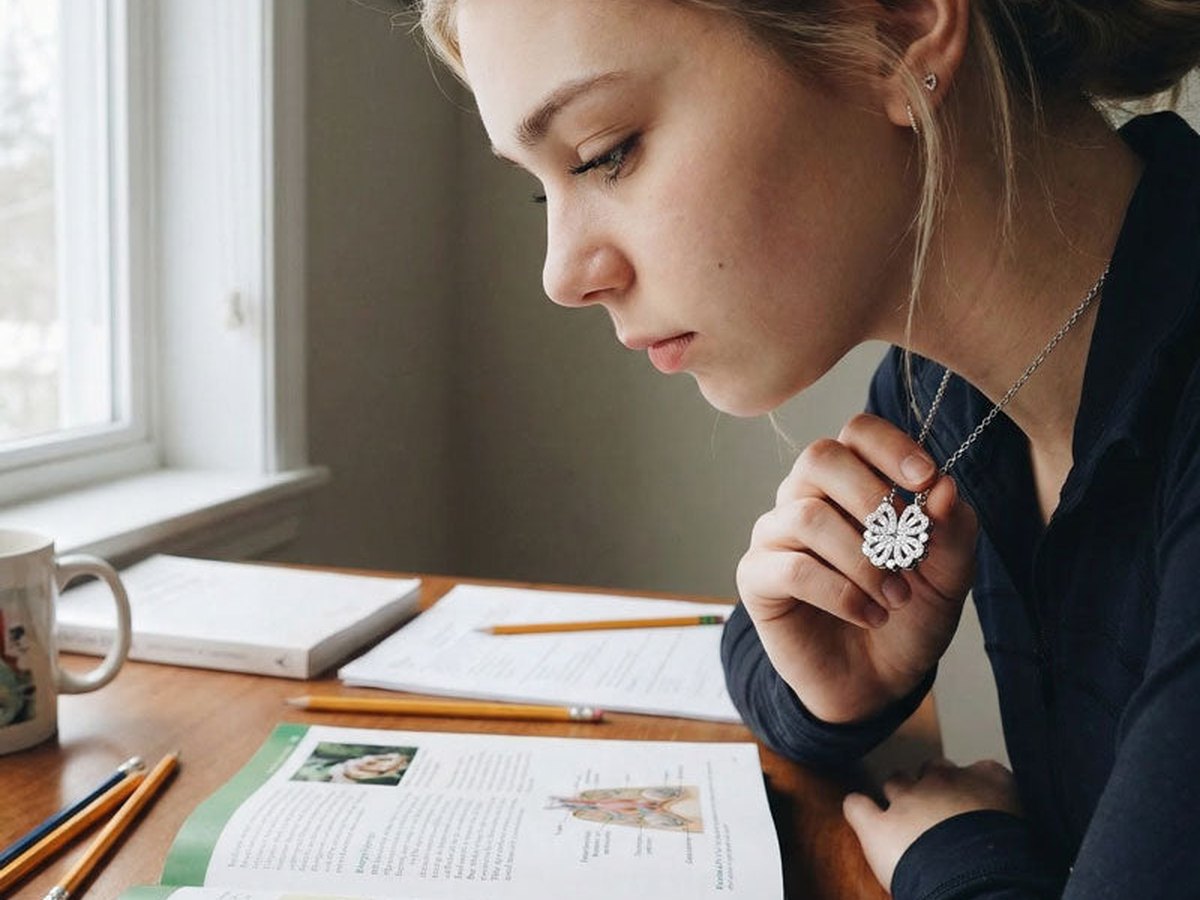 A teenage girl studying, holding the clover pendant at her neck